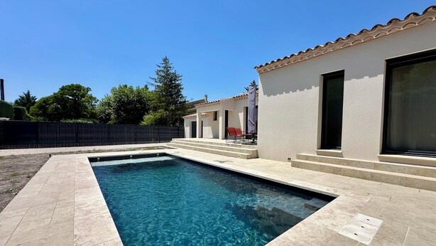 A rectangular swimming pool with clear blue water, surrounded by a tiled deck. There is a building with a tiled roof and large windows to the right. - Bastida Provença with private pool (Le Thor)