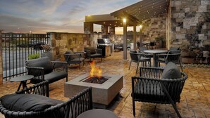 An outdoor patio with stone walls, wicker furniture, a fire feature, and a covered seating area. - Springhill Suites By Marriott Locust Grove (Locust Grove)