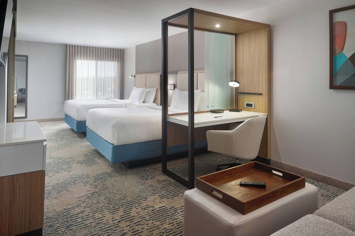 Habitación de hotel con dos camas, un escritorio, una silla, una mesita con bandeja y un espejo grande.