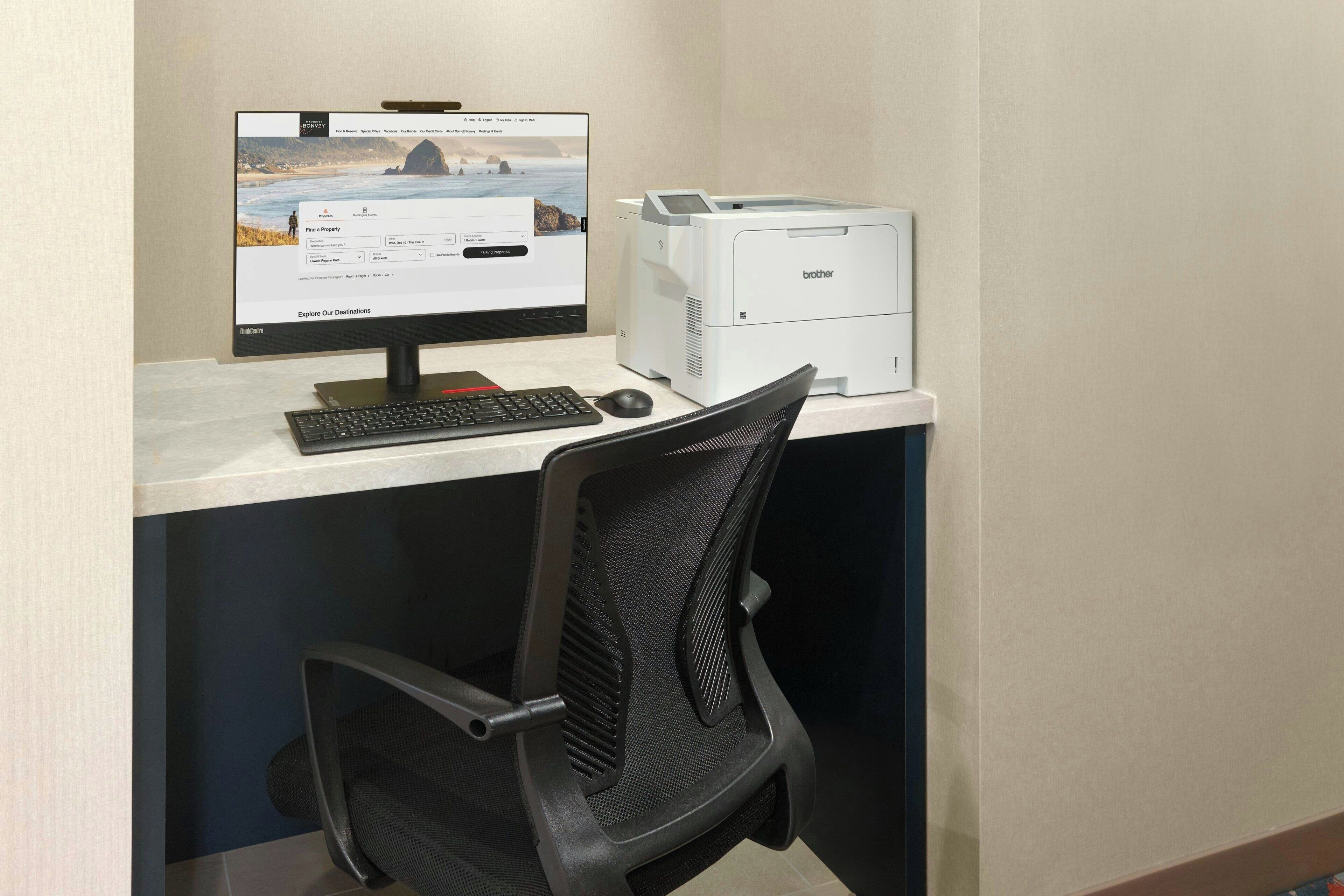 A computer desk with a monitor, keyboard, mouse, and a Brother printer.