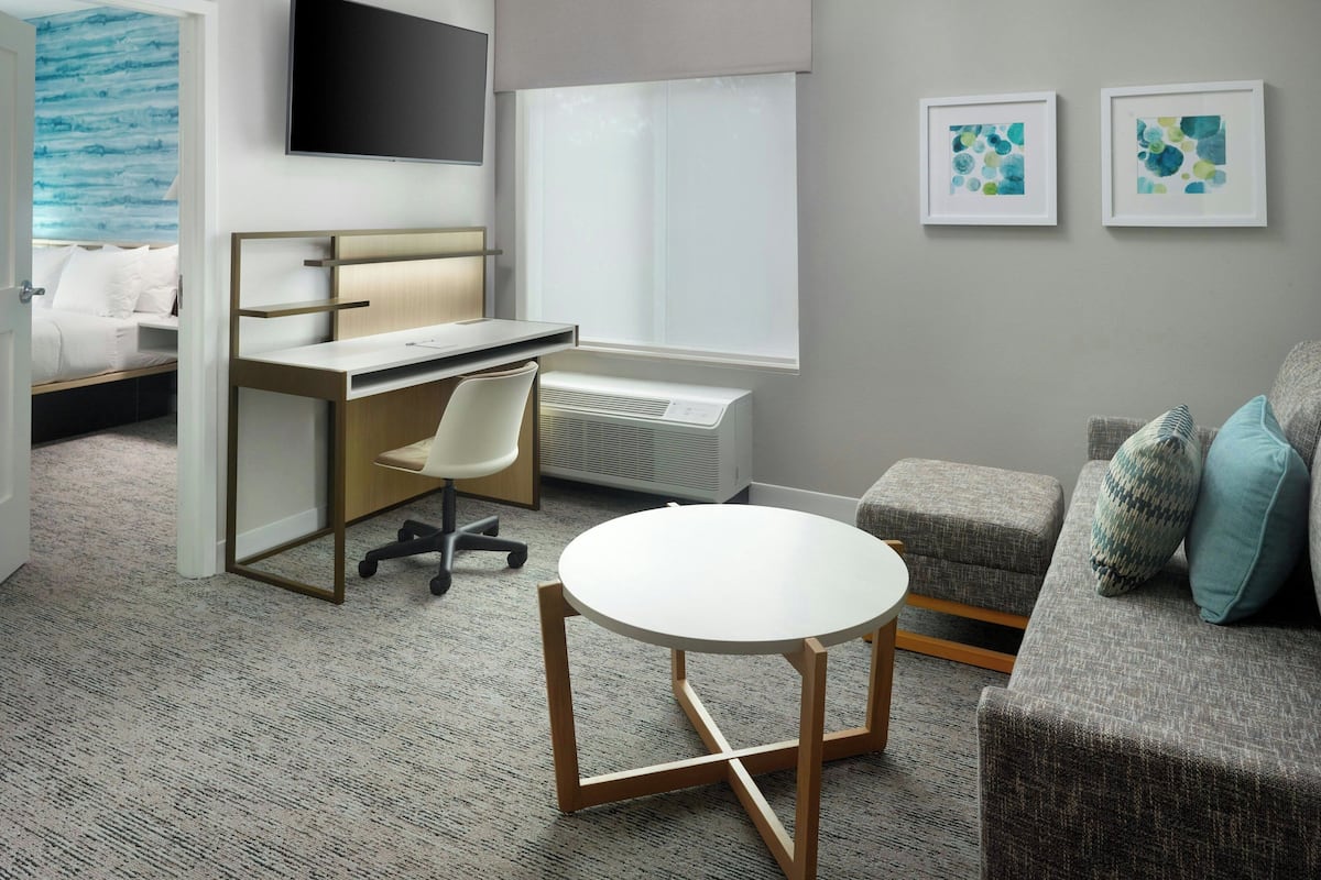 Una habitación de hotel moderna con cama, escritorio, silla, mesa redonda y sofá.