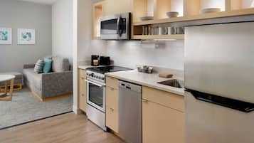 A modern kitchen with stainless steel appliances, a dishwasher, and a built-in oven. There is a dining area with a table and a sofa.
