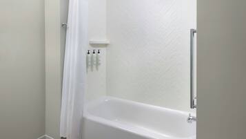 Une salle de bain avec une baignoire blanche, un rideau de douche et un mur recouvert de carreaux blancs.