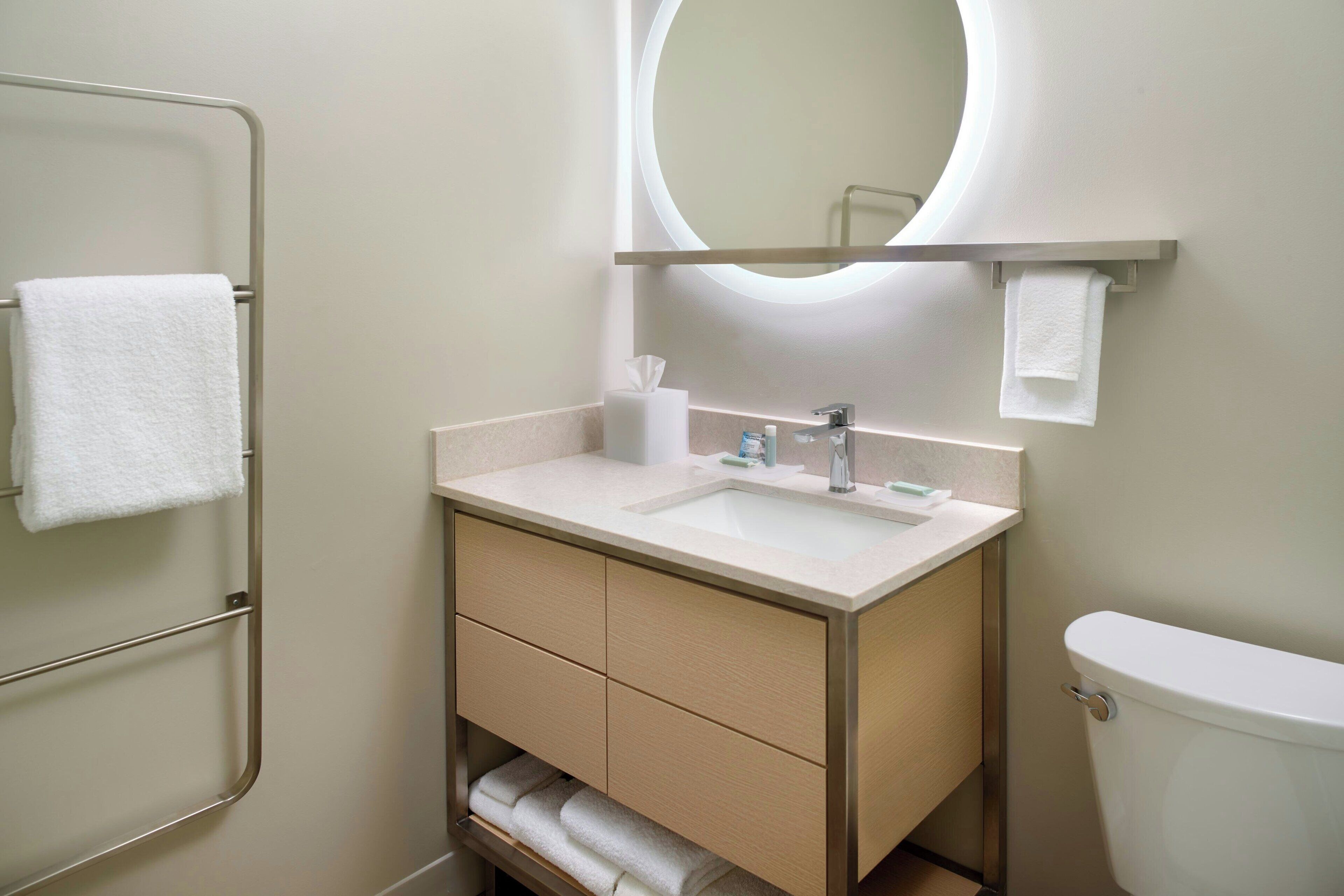 Un baño con inodoro, lavabo, espejo, toallero y dispensador de toallas.
