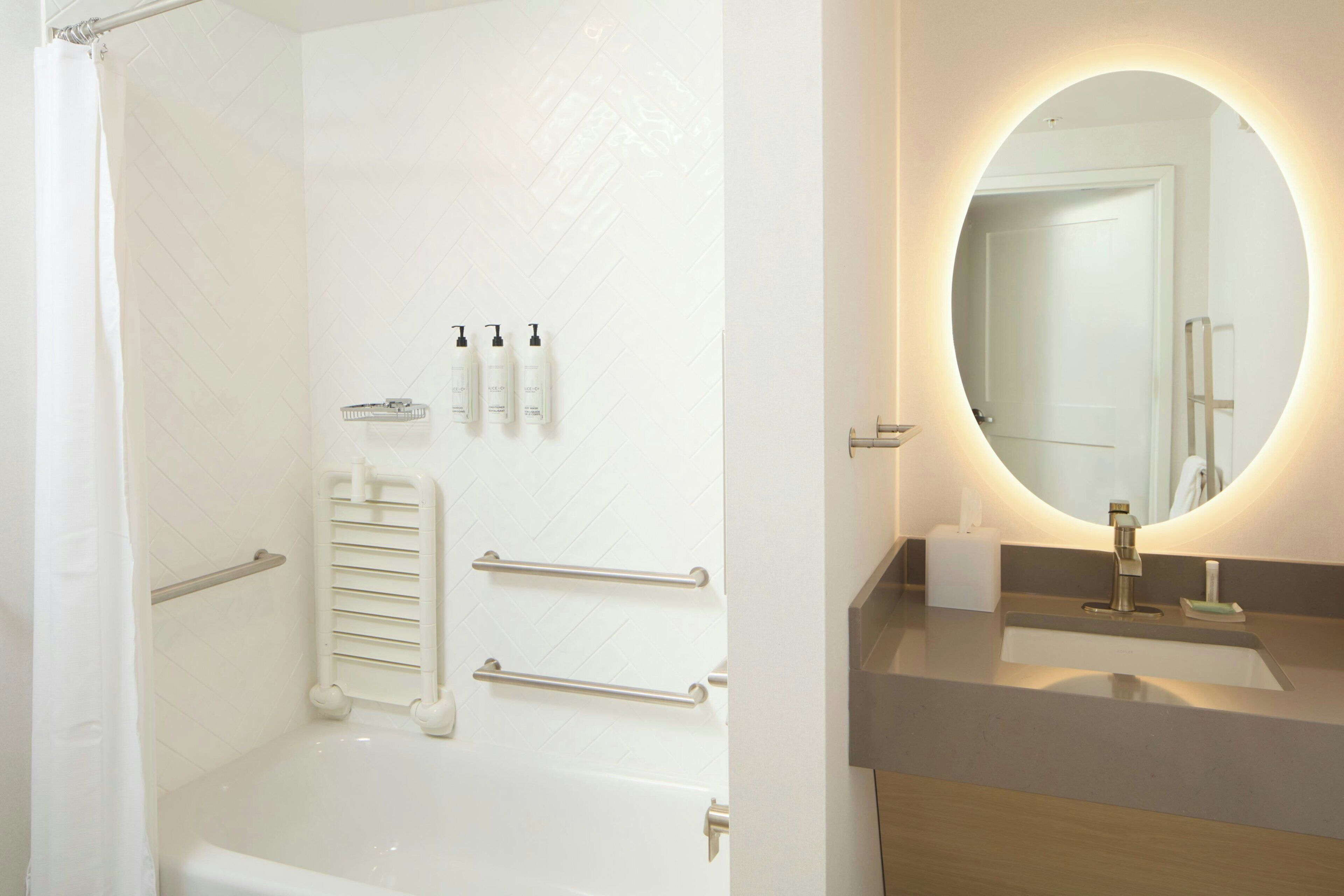Un baño moderno con bañera, cortina de ducha, toallero, secador de manos y un espejo con luz.