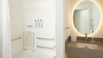 Un baño moderno con bañera, cortina de ducha, toallero, secador de manos y un espejo con luz.