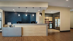 A hotel reception desk with a modern design, a self-service kiosk, and a market area with refrigerated display cases. - Towneplace Suites By Marriott Perry Georgia National Fairgrounds (Perry)
