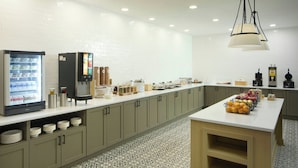 Une cuisine moderne équipée d’un espace de libre-service pour les boissons, d’un réfrigérateur rempli de lait et d’un assortiment de produits alimentaires disposés sur le comptoir.