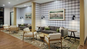 A modern lounge area with sofas, armchairs, and small tables, featuring checkered wallpaper and framed pictures on the walls. - Towneplace Suites By Marriott Perry Georgia National Fairgrounds (Perry)
