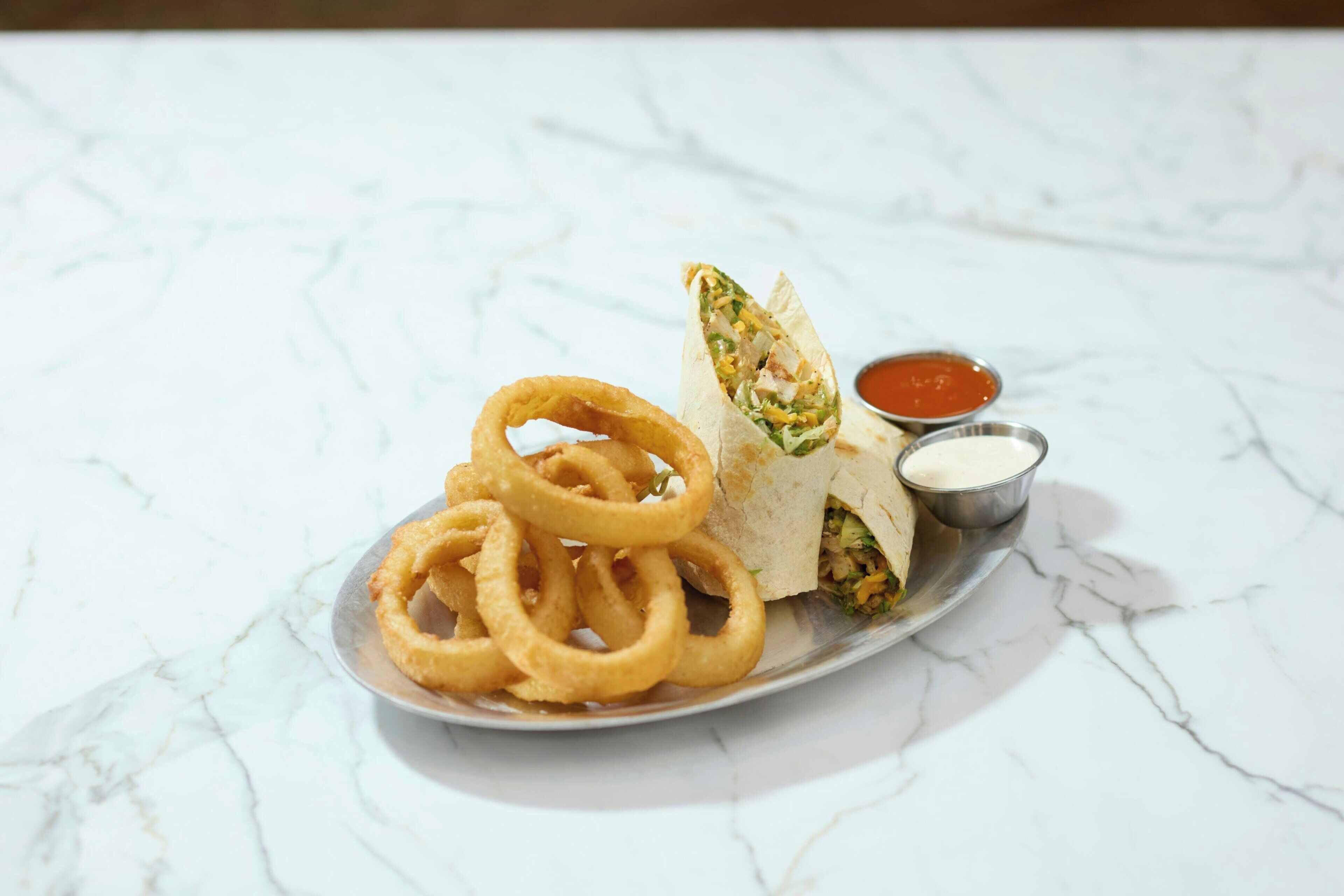 Une assiette comprenant un wrap, des rondelles d’oignon et deux sauces pour tremper.