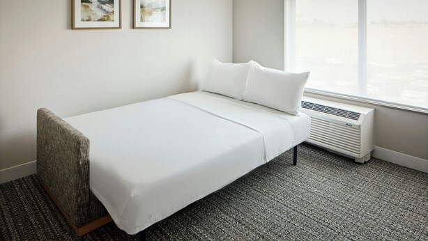 A single-bed room with a white bed, a window with a view, and two framed pictures on the wall. - Towneplace Suites By Marriott Perry Georgia National Fairgrounds (Perry)