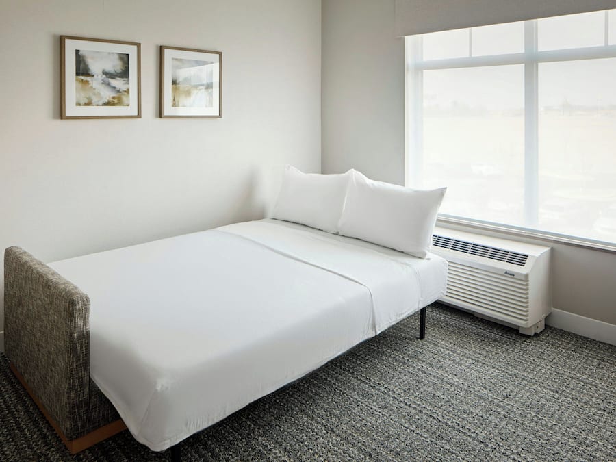 A single-bed room with a white bed, a window with a view, and two framed pictures on the wall.