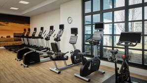 A gym with various exercise machines, a clock on the wall, and large windows.