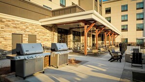 An outdoor patio area with two barbecue grills, seating, and a covered walkway. - Towneplace Suites By Marriott Perry Georgia National Fairgrounds (Perry)