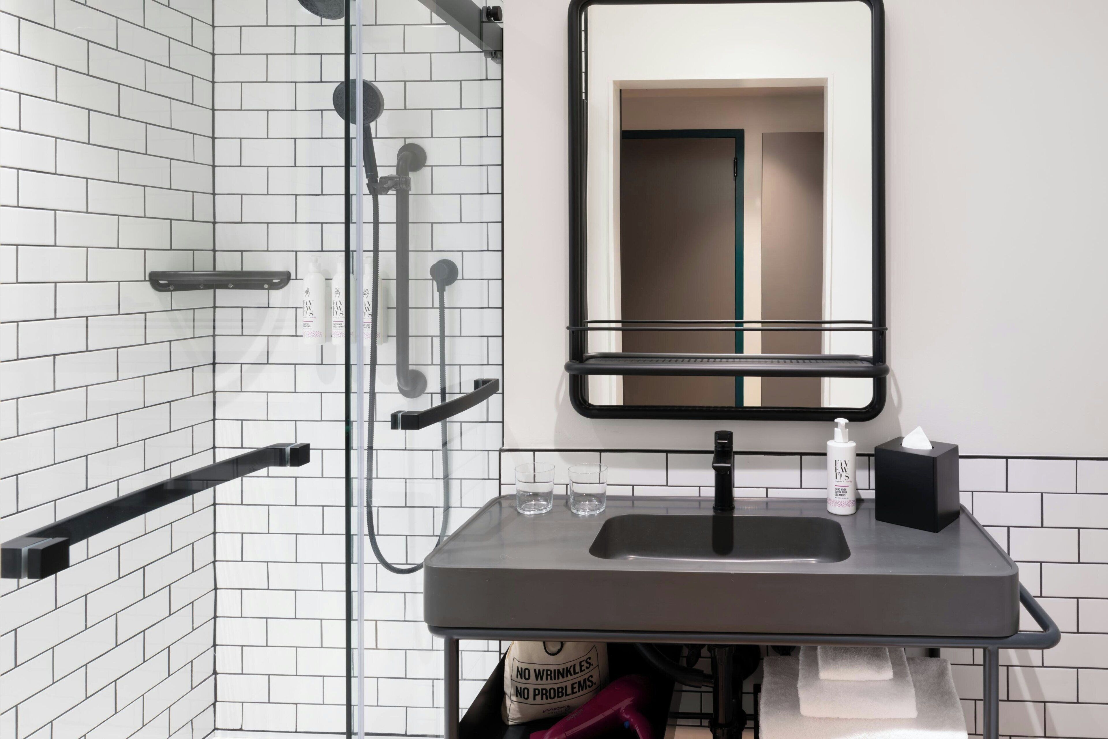 A modern bathroom with white tiled walls, a black sink, and a mirror.