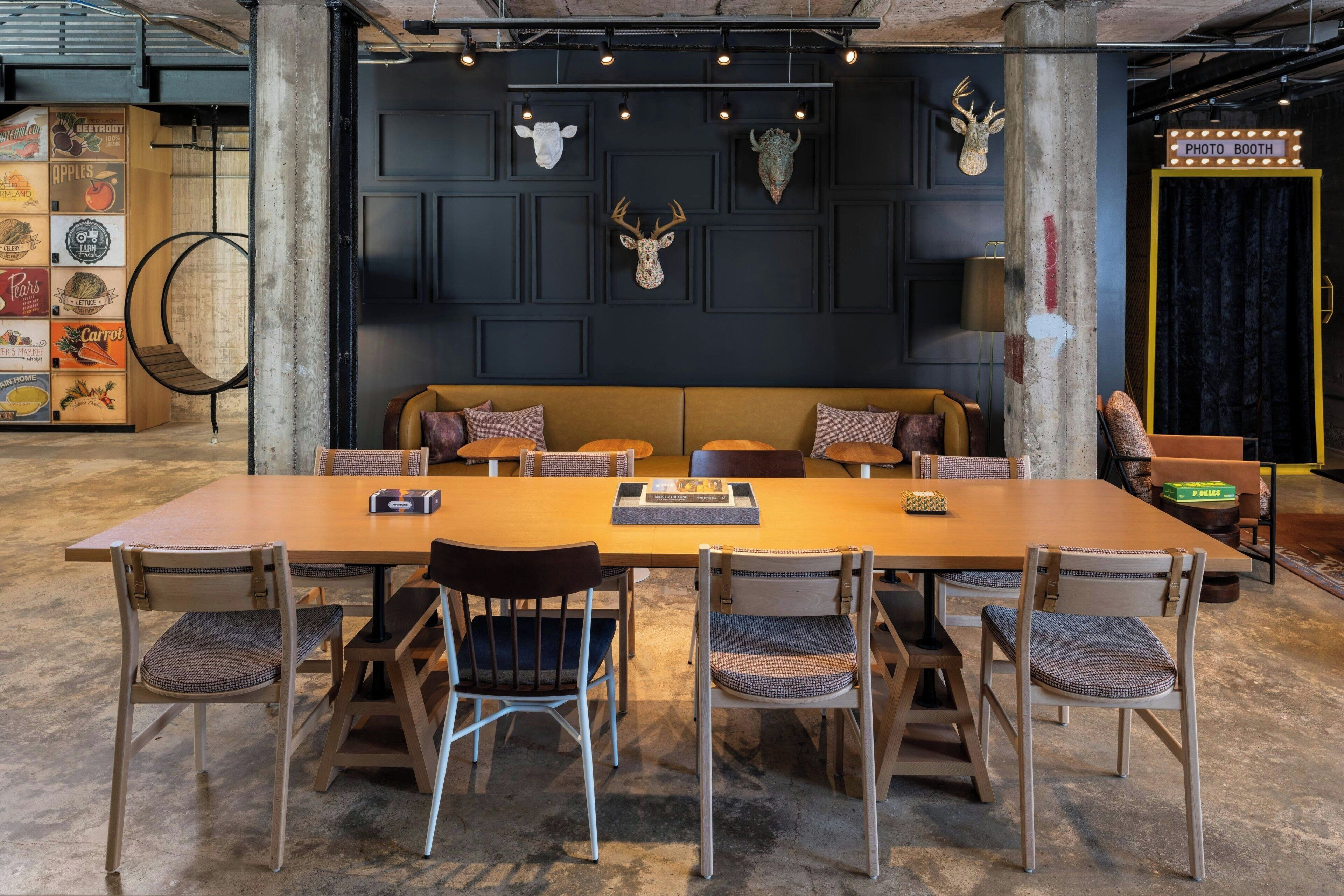 Ein modernes Interieur mit einem langen Holztisch, umgeben von Stühlen, einer Couch mit Kissen und dekorativen Geweihköpfen an der Wand.