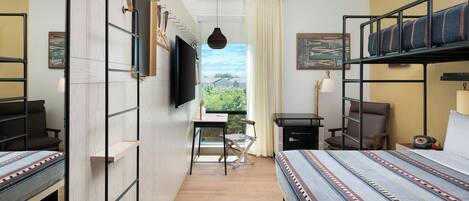 Habitación de hotel con literas, un escritorio, una silla, televisión y ventana con vista a zonas verdes.