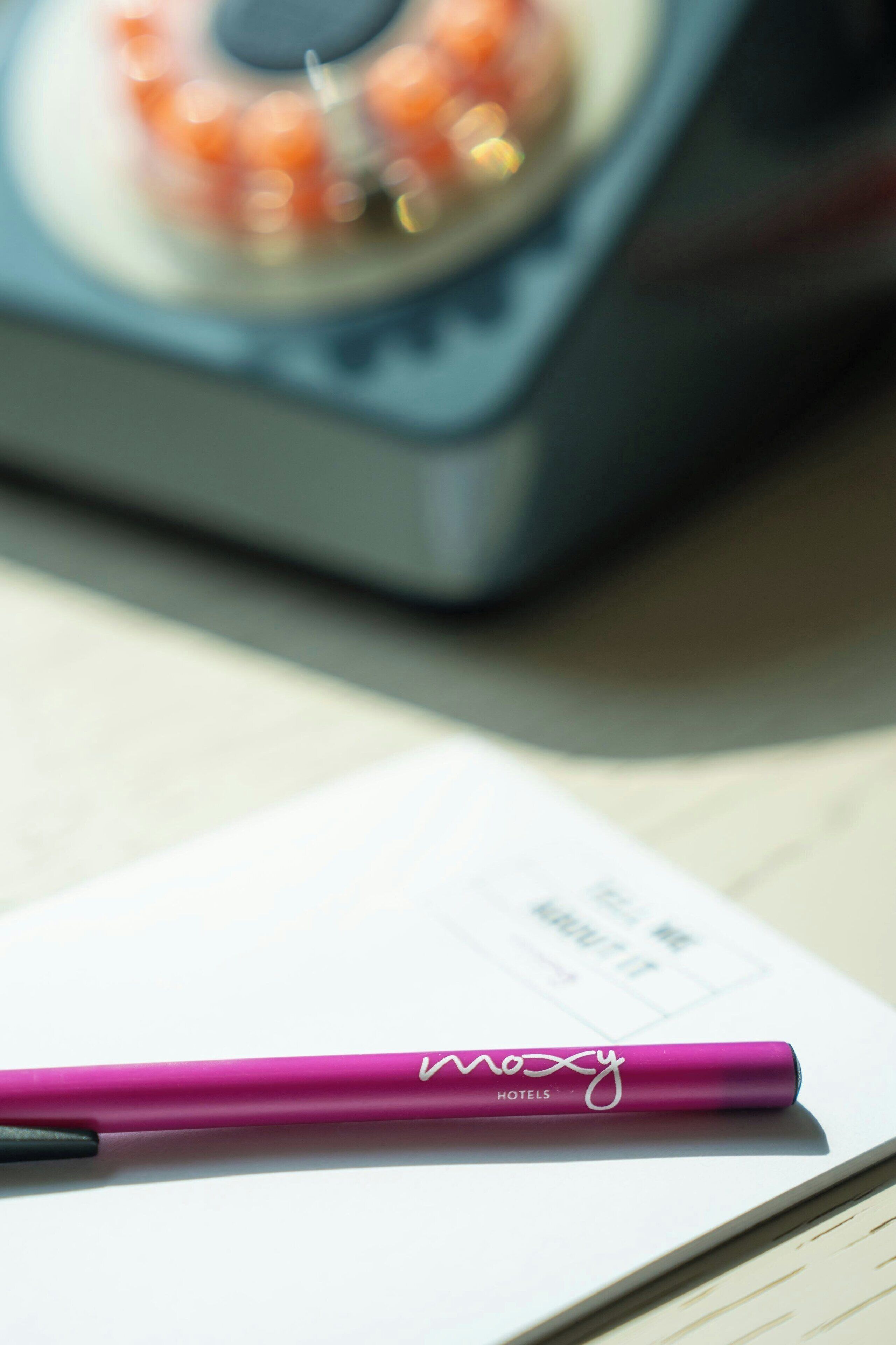 A notebook with a pink pen on top, placed on a wooden surface.