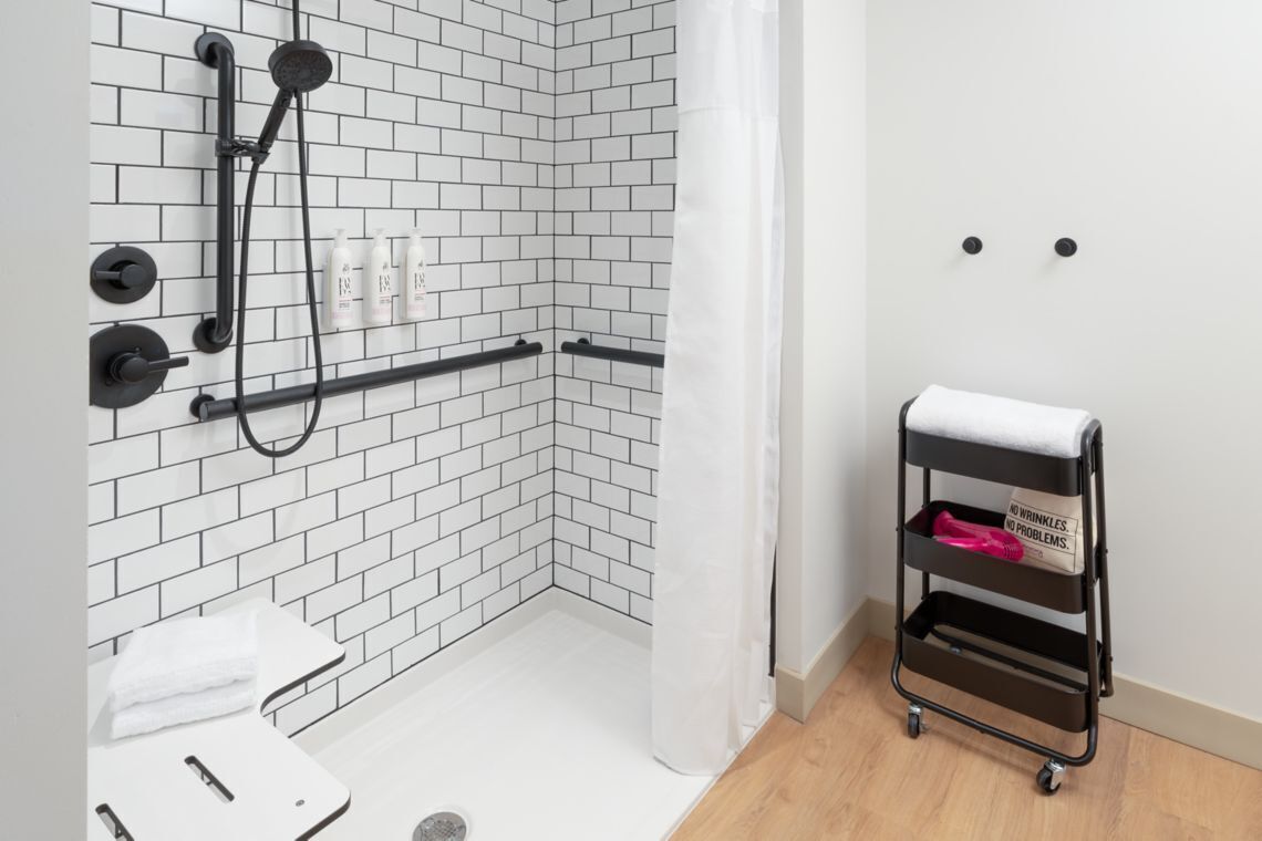 Un bagno moderno con zona doccia rivestita di piastrelle bianche, un portasciugamani nero e una tenda da doccia bianca.