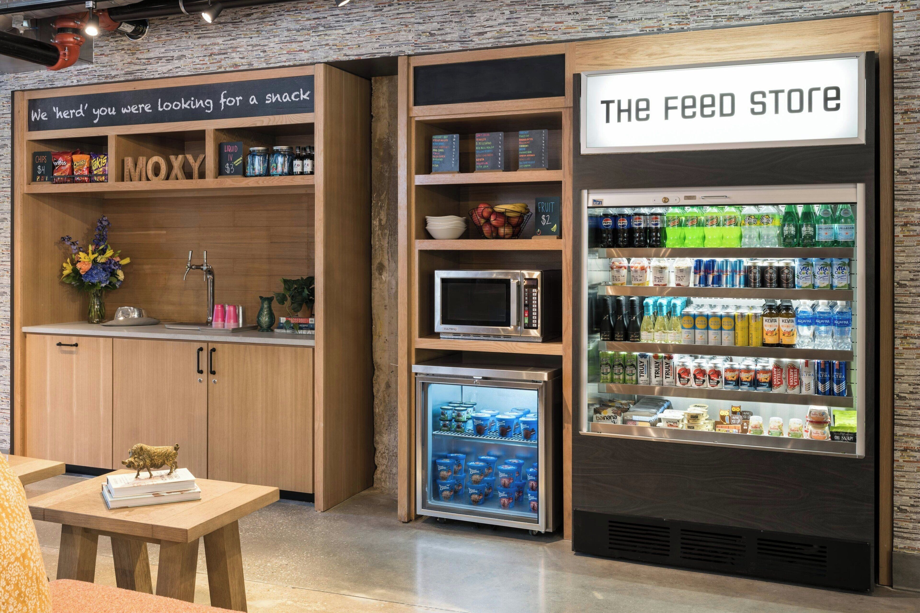 A snack bar with a microwave, refrigerator, and shelves stocked with snacks and beverages.