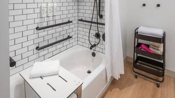 Une salle de bain moderne avec une baignoire blanche, des barres d’appui noires, une serviette blanche et un chariot contenant une autre serviette et un panneau.