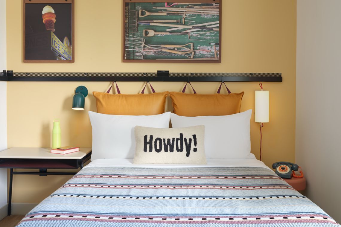 Une chambre d’hôtel comprenant un lit, une table de chevet, une lampe, un téléphone et une œuvre d’art murale.