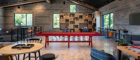 A spacious room with a large chess table, multiple seating areas, and large windows providing natural light.