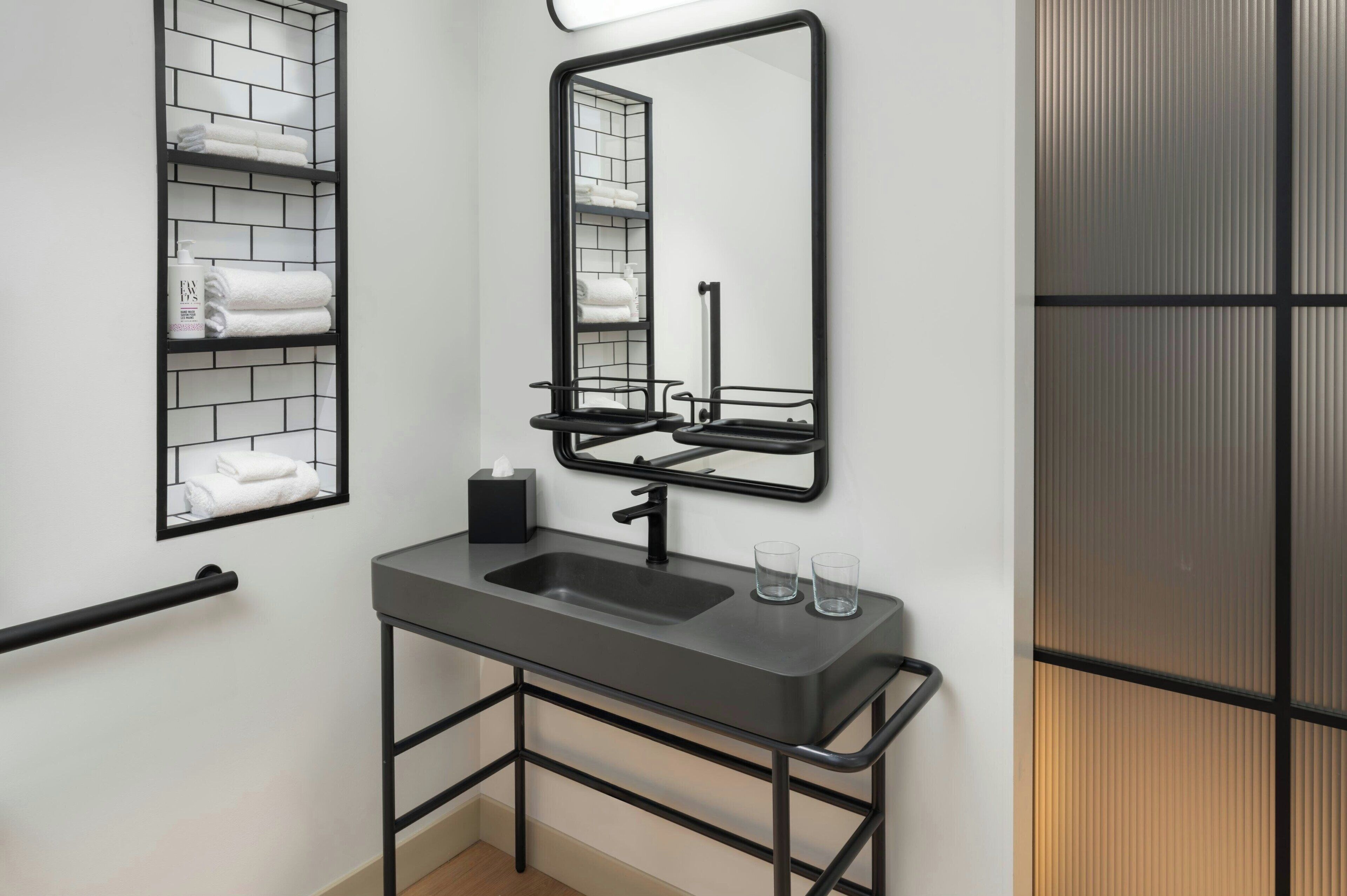 Un baño moderno con un lavamanos de metal negro, un espejo y un perchero con toallas dobladas.