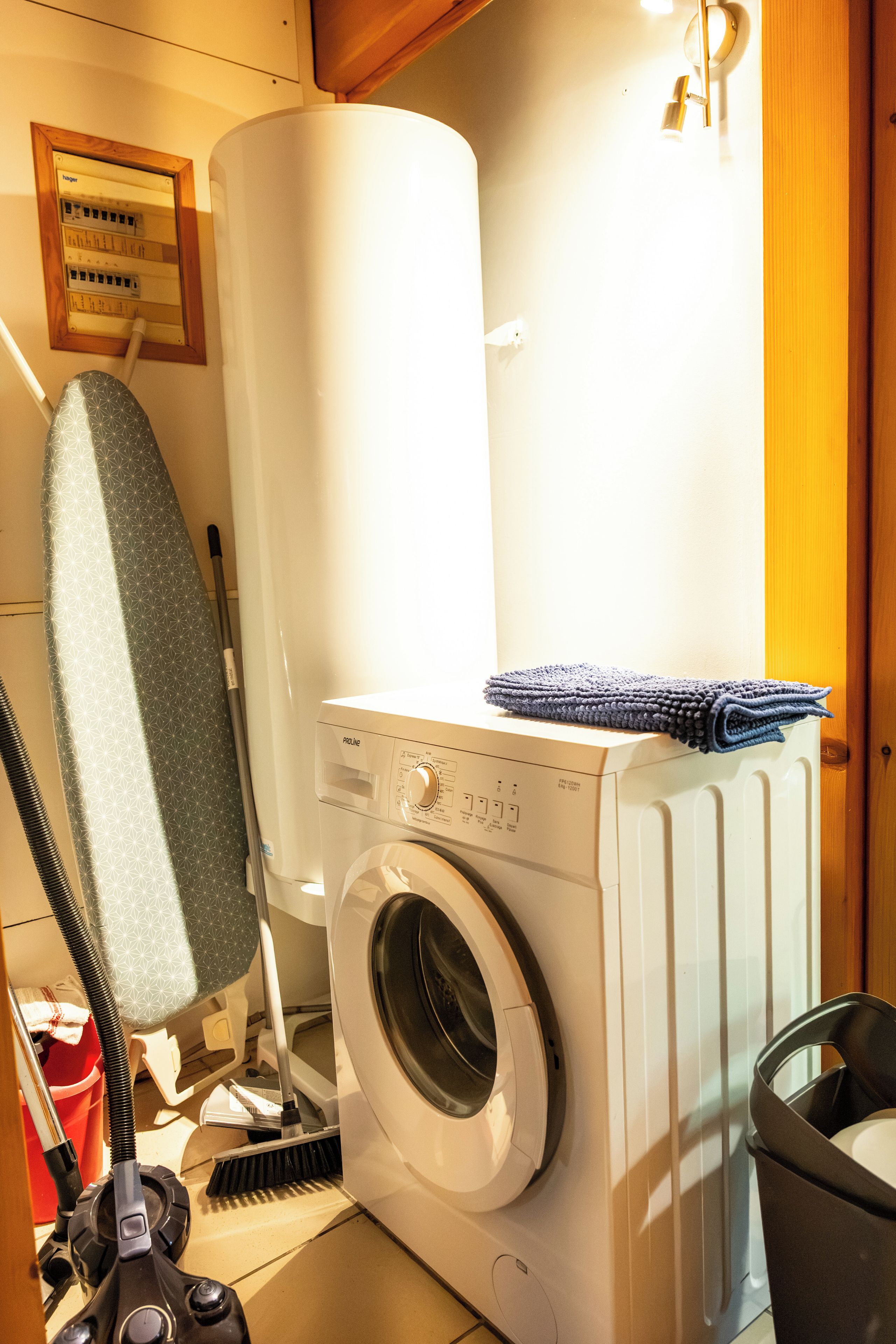 Un espace buanderie compact comprenant un lave-linge à chargement frontal, un étendoir et un aspirateur.