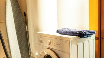 Un espace buanderie compact comprenant un lave-linge à chargement frontal, un étendoir et un aspirateur.