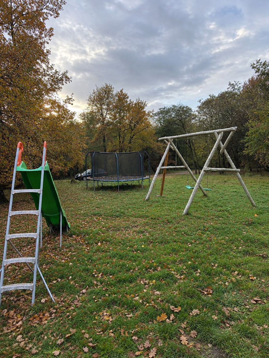 A grassy outdoor area with a swing set, a slide, and a trampoline.