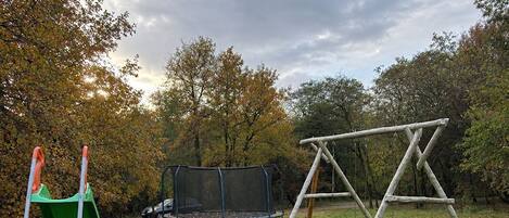 Un espacio al aire libre con césped, un parque infantil con columpio, tobogán y cama elástica.