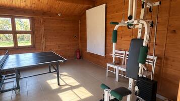 Une salle de sport équipée de matériel d’exercice, d’une table de ping-pong et d’une fenêtre donnant sur un espace verdoyant.