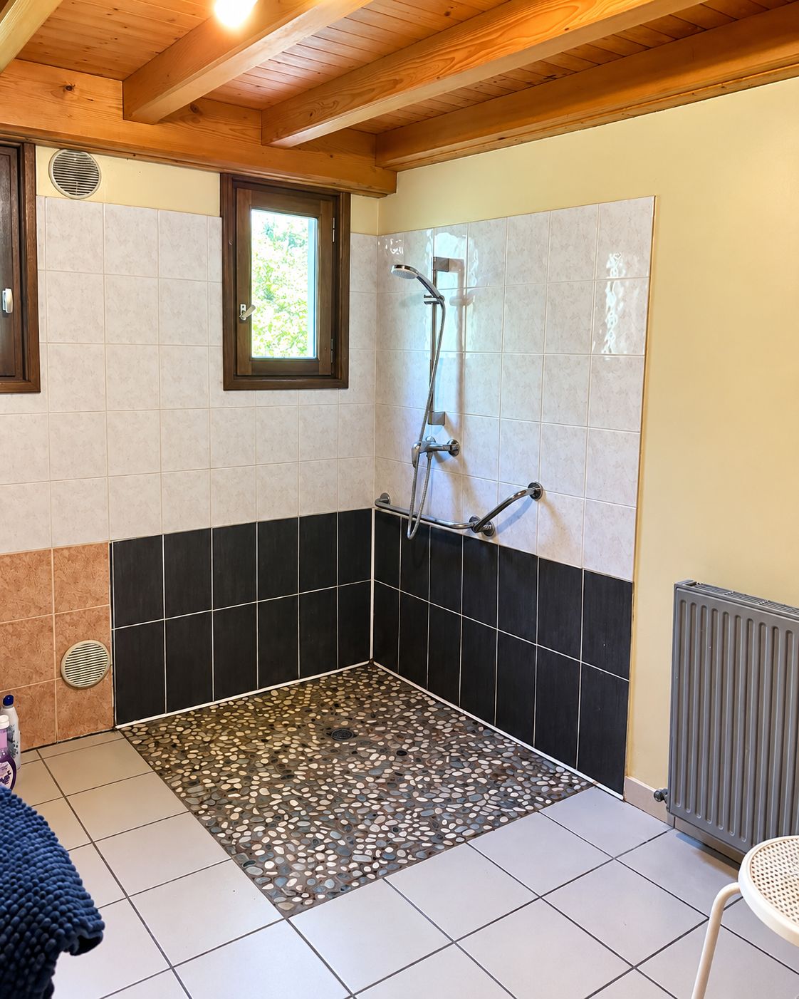 Un espace douche avec un sol carrelé, une fenêtre et un radiateur.