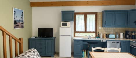 Un espacio habitable pequeño con kitchenette, un sofá con funda estampada de hojas y una mesa de comedor con sillas.