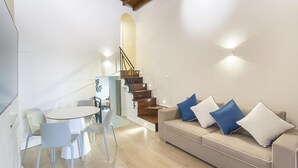 En moderne stue med sofa, spisebord med stole og trappe op til et højere plan.