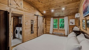 Een slaapkamer in een houten chalet, met een bed, een wasmachine en een raam met gordijnen.