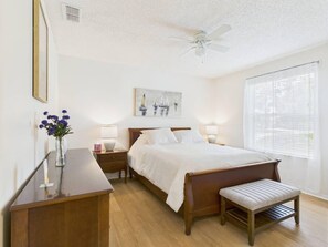 A bedroom with a bed, bedside tables, a desk, a chair, a ceiling fan, and a window with blinds. - Relaxing Rio Ranchero House with Golf Cart (Lady Lake)