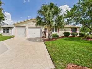 A two-story house with a garage, a well-maintained lawn, and a palm tree. - Relaxing Rio Ranchero House with Golf Cart (Lady Lake)