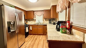 Una cocina con armarios de madera, un refrigerador de acero inoxidable, un horno empotrado y una encimera con una cafetera y cajas.