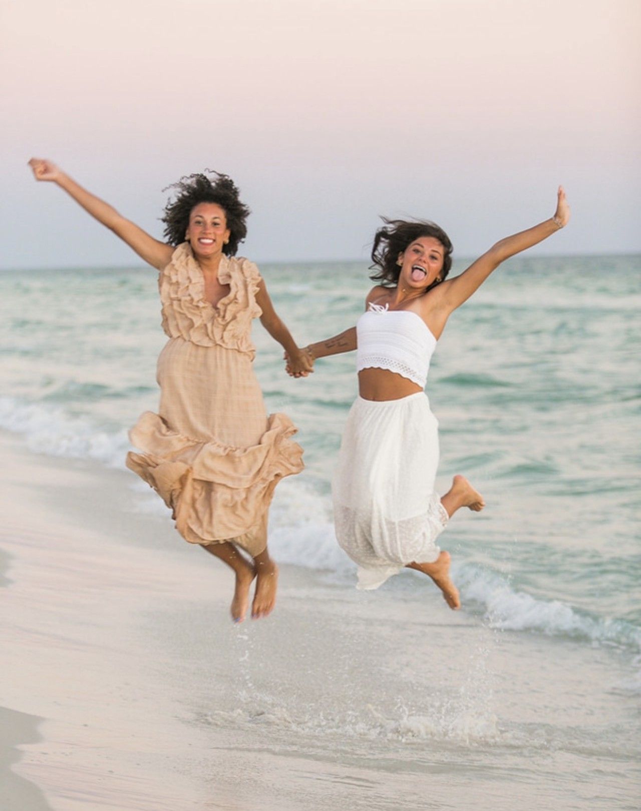 Two people jumping on a beach with ocean in the background.