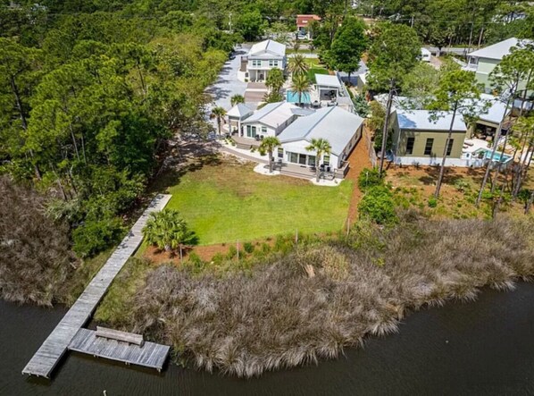 A coastal property with a dock, a grassy lawn, and a cluster of houses surrounded by dense vegetation.