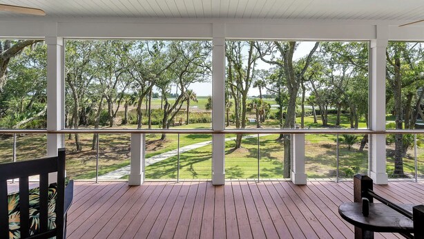 Un espace extérieur abrité doté d’une terrasse en bois, de grandes fenêtres et d’une vue sur un jardin aménagé.