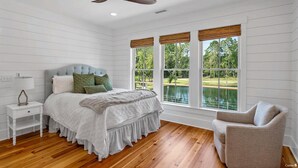 Une chambre à coucher comprenant un lit, une table de chevet, une chaise et de grandes fenêtres donnant sur un lac.
