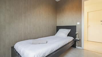Un lit simple avec une tête de lit sombre, dans une pièce dont les murs sont recouverts de panneaux de bois.