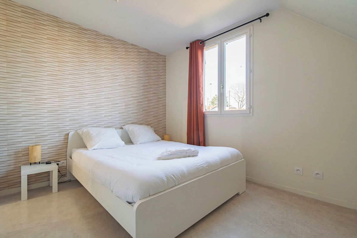 A bedroom with a bed, a nightstand, a window with curtains, and a wall with a textured pattern.