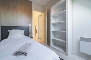A modern bedroom with a neatly made bed, a walk-in closet, and a built-in heater. - Maison Harmonie by MM Suites (Cormontreuil)