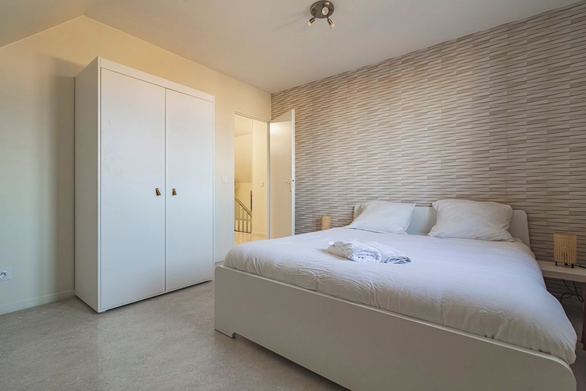 A bedroom with a large bed, a wardrobe, and a wall with a textured pattern.