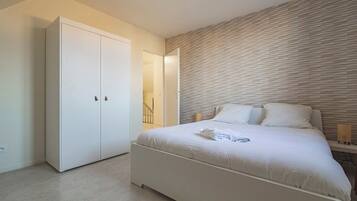 A bedroom with a large bed, a wardrobe, and a wall with a textured pattern.