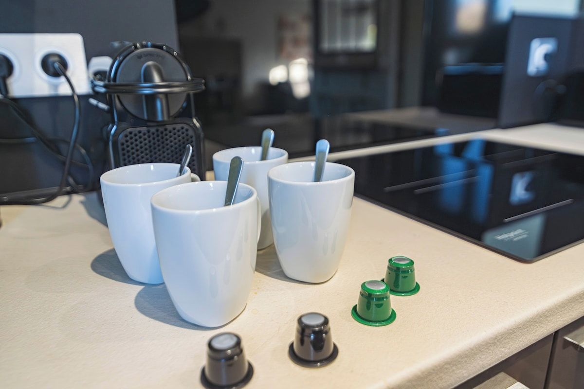 En bordplade i køkkenet med fire hvide kopper, en kaffemaskine og nogle grønne og sorte knapper.